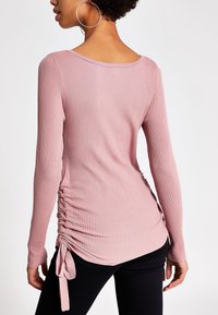 Rosa geripptes Langarmtop mit rundem Ausschnitt. Verfügt über Raffung mit Bindebändern an der Hüfte und eine taillierte Silhouette.