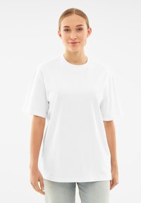 Biała bawełniana koszulka z okrągłym dekoltem i krótkimi rękawami, charakteryzująca się luźnym krojem i gładką fakturą. Brak widocznych wzorów lub akcentów.