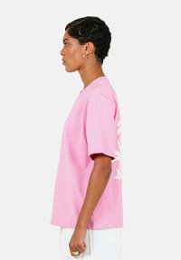 Roze t-shirt met korte mouwen en een ronde halslijn, met een gestructureerd wit grafisch ontwerp op de rug. Gemaakt van zacht katoen.