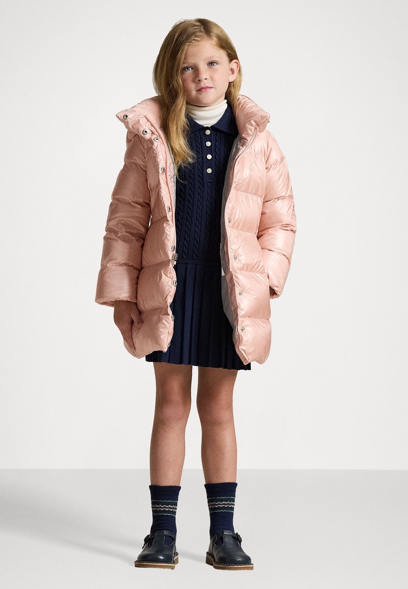 Light pink puffer jacket with a high collar, navy ribbed dress, knee-length, and navy socks with a green and white pattern, worn with black shoes.