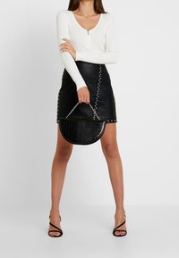 Top bianco a maniche lunghe a costine con zip, gonna nera in ecopelle con borchie argentate e borsa nera a mezzaluna con manico a catena.