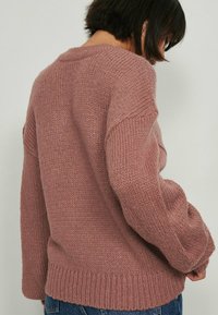 Różowy dziergany sweter o luźnym kroju, z teksturowanym wykończeniem, prążkowanym dołem i szerokimi rękawami. Widok z tyłu ukazuje dekolt i szwy.