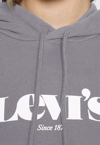 Felpa grigia con tasca frontale. Presenta un cappuccio con coulisse e un grande logo stampato bianco "Levi's" con "Dal 1873" sottostante. Tessuto morbido.