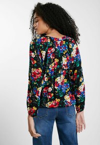Blumenbluse mit schwarzem Hintergrund, verziert mit bunten roten, blauen und gelben Blumen, langen Ärmeln und einem gerafften Rückendetail.