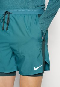 Teal Nike löparshorts med dragsko i midjan, sidofickor och vit logotyp. Tillverkade av ett lätt, strukturerat material.