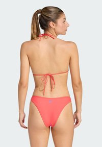 Różowa bikini z wiązaniem z tyłu i minimalnym pokryciem. Gładka tekstura, regulowane ramiączka oraz małe logo na tyle majtek.