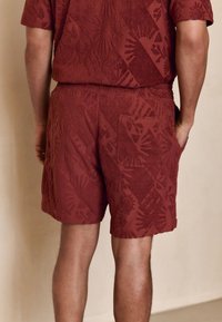 Shorts rossi con trama testurizzata e motivo a soli e forme geometriche; vita elasticizzata; unica tasca posteriore.