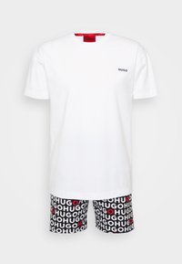 T-shirt en coton blanc avec logo "HUGO" noir sur la poitrine ; associé à un short noir présentant un texte "HUGO" répété et des accents de cercles rouges.