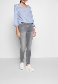 Top de rayas azul y blanca con hombros al aire, combinado con jeans skinny grises y zapatillas blancas. Cuenta con puños con lazos y un corte casual.