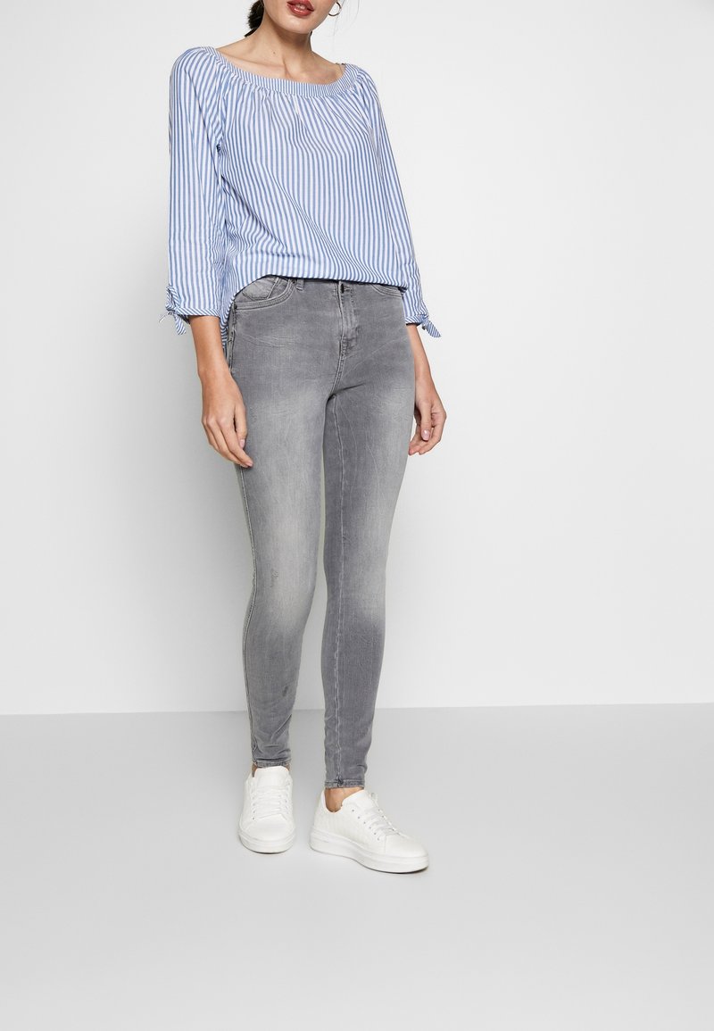 Top de rayas azul y blanca con hombros al aire, combinado con jeans skinny grises y zapatillas blancas. Cuenta con puños con lazos y un corte casual.