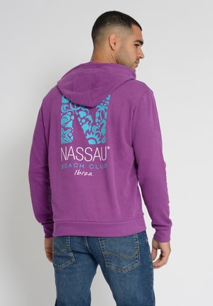 Paarse hoodie met een blauw bloemenpatroon "NASSAU" logo op de achterkant. Heeft een trekkoord in de capuchon en ribgebreide manchetten, gecombineerd met spijkerbroek.
