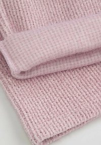 Miękka różowa dzianina z prążkowanym wzorem, złożona w taki sposób, aby pokazać gładką wewnętrzną stronę i puszystą zewnętrzną stronę.