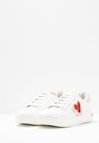 Vita lädersneakers med en fluffig krämfärgad krage, som har en röd paljettprydd hjärtdekor på sidan och vita snören.