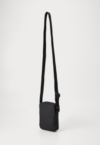 Sort crossbody taske med rektangulær form, glat stof, justerbar webstrap og lynlås lukning. Enkel design med minimale detaljer.