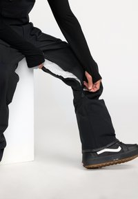 Zwarte sneeuwbroeken met een ritssluiting ventilatie en mesh voering, gecombineerd met zwart-witte sneakers. Glad materiaal en een comfortabele pasvorm.