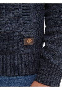 Navy Strickpullover mit gerippten Bündchen und Saum, ausgestattet mit einem Lederlogo-Patch, das an der Seite "Peirrot Industries" trägt.