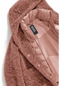 Cappotto fuzzy e texture in rosa tenue con un morbido interno isolato. Presenta bottoni a scatto e un'etichetta del marchio all'interno.