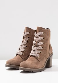 Ruske nahkaläpet, joissa on paksut korot, beige- ja valkoiset paksut nauhat sekä sivuvetoketjut valkoisella pinnalla.