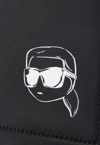 Černá tkanina obsahuje bílý grafický prvek stylizované tváře se slunečními brýlemi, minimalistický design, hladký povrch a žádné další detaily.