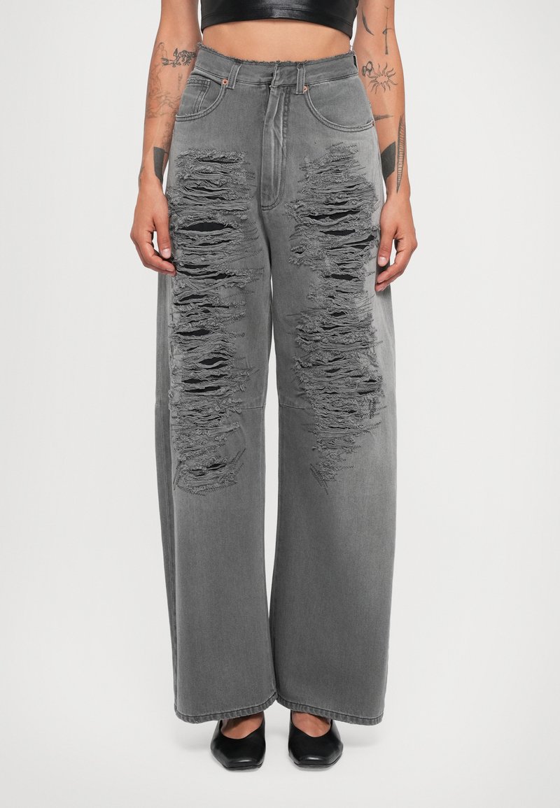 Grå vida jeans med framträdande slitningar på båda benen, hög midja och en slät denimtextur. Svart fotbeklädnad fulländar looken.