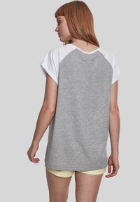 Grå t-shirt med hvide raglanærmer, der har en afslappet pasform og blødt stof. Bagpå ses en rund halsudskæring og minimale designelementer.