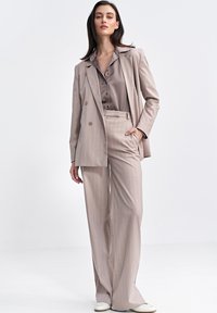 Beżowy garnitur w prążki składający się z marynarki podwójnie zapinanej i spodni o szerokich nogawkach. Gładka tkanina z satynową bluzką pod spodem.