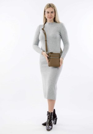 Grijze, aansluitende gebreide jurk met lange mouwen; gecombineerd met een kleine bruine crossbody tas met ritsen en een lange, verstelbare schouderband. Zwarte enkelboots.