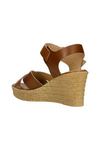Sandale à talon compensé en cuir marron avec une semelle en jute de style espadrille, dotée de larges sangles et d'une fermeture à boucle réglable au niveau de la cheville.
