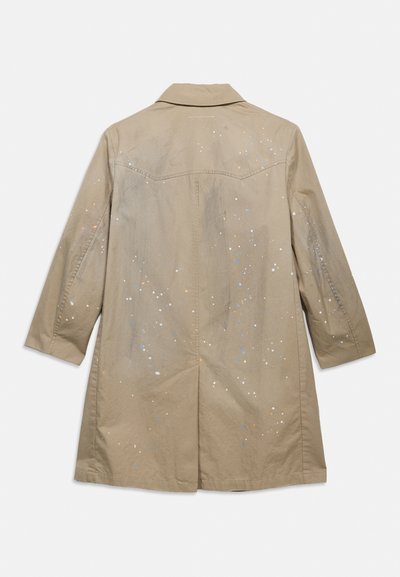 Μπεζ μακρύ παλτό με γιακά, εμφανιζόμενο από πίσω, με διακριτικές πολύχρωμες πινελιές βαφής στο ύφασμα.