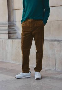 Pantaloni din catifea călduță, cu o croială lejeră, având pliuri la față, asortați cu adidași albi și un pulover lung teal.