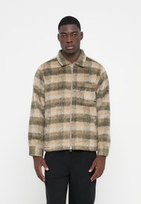 Plaid zip-up jacket in beige and green tones, featuring a soft texture and a collared neckline, with side pockets and ribbed cuffs.