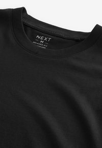 T-shirt nera in cotone morbido con vestibilità rilassata, colletto a girocollo, dettagli di cucitura minimal e un'etichetta con il nome del marchio e la taglia.