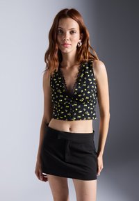 Svart crop top med gul blomstertrykk, blondekant og knappelukking; kombinert med et svart mini-skjørt. Glatt stofftekstur.