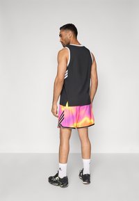 Pánsky športový outfit pozostávajúci z čierneho tielka bez rukávov a živých krátkych nohavíc s tie-dye vzorom v ružovej, oranžovej a žltej farbe s čiernymi doplnkami.