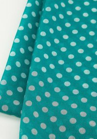 Turkusowa tkanina w białe kropki, o gładkiej fakturze i lekkim materiale, układająca się w miękkie fałdy na jasnym tle.