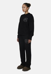 Zwart gebreid sweater- en broekset met een logodetail op de borst en dij; relaxte pasvorm, ribbelboorden en zachte textuur.