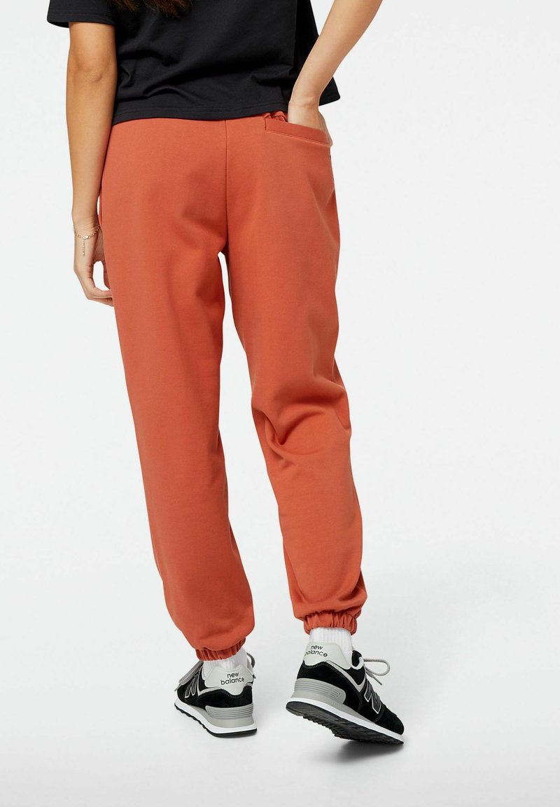 Orange Sweatpants mit lässiger Passform, elastischem Bund und Bündchen. Kombiniert mit schwarzen Sneakers mit weißen Akzenten und Schnürsenkeln.