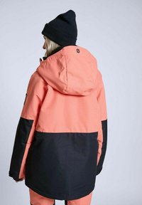 Pink og sort vandtæt jakke med hætte, med en tekstureret overflade og kontrasterende farveblokdesign. Sort strikket hue bæres.