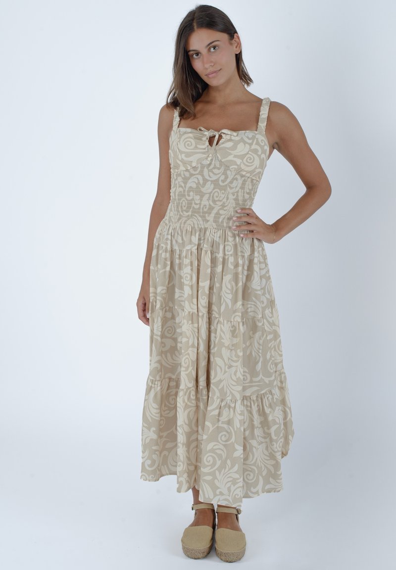 Jasno beżowa sukienka z kwiatowym wzorem, kwadratowym dekoltem i wiązaniem. Posiada marszczoną talię i warstwową spódnicę. Noszona z butami espadrilles.