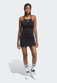 Black bodycon dress with thin straps, featuring white side stripes. Paired with white sneakers and striped socks. Smooth fabric texture.