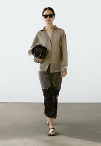 Lichtbeige overhemd met knopen, donkergrijze rok met zwarte franjes, zwarte tas en sandalen met zilveren accenten. Minimalistisch ontwerp, gladde texturen.