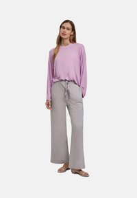 Lichtpaars langemouw shirt gecombineerd met losse lichtgrijze broek. De broek heeft een trekkoord in de taille, wat zorgt voor een comfortabele pasvorm.