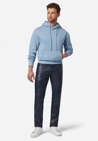 Lichtblauwe hoodie met een voorzak, gecombineerd met donkerblauwe leren broek en witte sneakers, met een losse pasvorm en schuurlintjes.