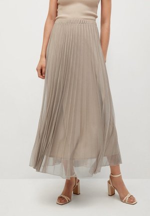 Kvinde iført en beige plisseret midi nederdel med en ribbet top og beige højhælede sandaler på hvid baggrund.