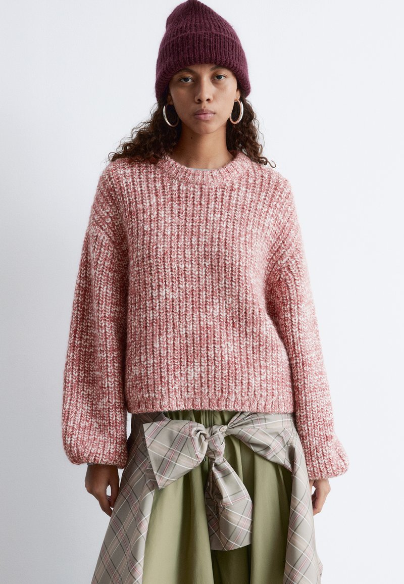 Gestickter Pullover in Rosa und Weiß mit einem strukturierten Muster, Rundhalsausschnitt und langen, oversized Ärmeln, kombiniert mit einem hellgrünen Rock und einer Schleife.