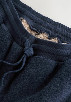 Navy blue sweatpants feature a soft inner lining, ribbed waistband, and a tied drawstring for adjustment. Textured fabric adds warmth.