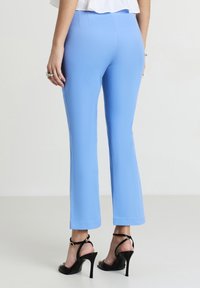 Pantaloni svasati azzurro chiaro realizzati in tessuto morbido, con vita alta e finitura pulita. Abbinati a sandali neri con tacco alto e straps.