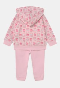 Set di felpa e pantaloni rosa. La felpa presenta una stampa di orsetti su tutta la superficie e tasche frontali. I pantaloni sono di un rosa uniforme con polsini elastici. Materiale morbido.