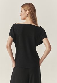 Sort, løstsiddende top med bred halsudskæring, korte ærmer og en subtil glitrende tekstur. Glat stof med en afslappet silhuet.