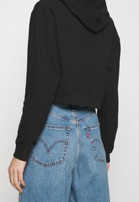 Hoodie nera corta con maniche lunghe, abbinata a jeans a vita alta di coloreazzurro chiaro con cuciture visibili e tasche posteriori.